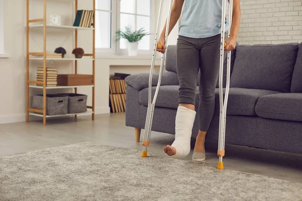 Woman with broken injured leg in cast standing with metal crutches during rehabilitation at home