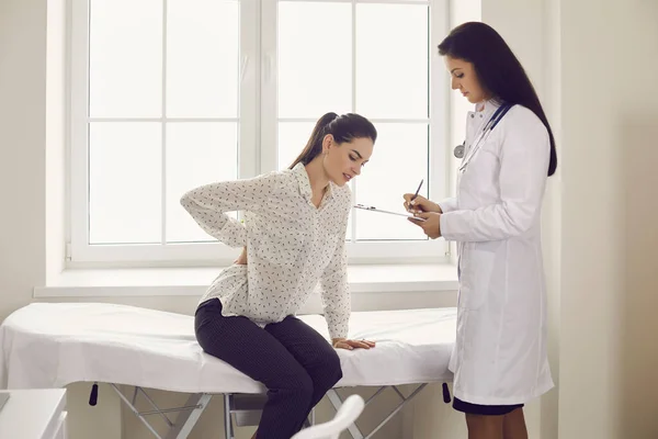 Mulher infeliz reclamando de dor nas costas sentado na cama de exame no consultório médico — Fotografia de Stock