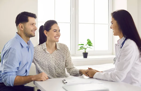 Glückliches Paar und Hausarzt am Tisch, Händchen haltend und lächelnd — Stockfoto