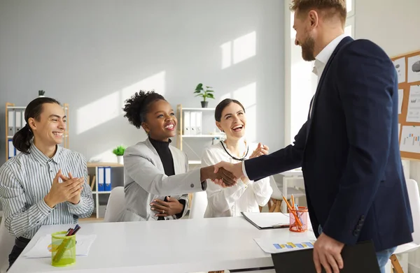 Young multiracial business team shakes hands with a man welcoming him as a new team member.