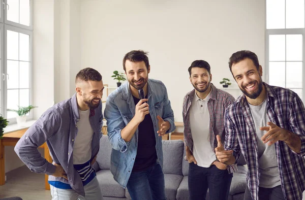 Positieve vrolijke mannelijke vrienden zingen favoriete liedjes op karaoke microfoon samen tijdens home party — Stockfoto