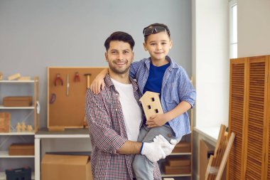 Baba ve oğlunun atölyedeki portresi. Aile tasarımı ve ahşap bir ev modeli.