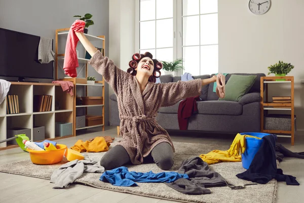 Tired housewife crying while cleaning up mess and picking up scattered clothes from floor
