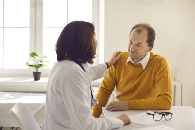 Doktor, kliniğe yaptığı ziyarette hastalarına destek olmak ve güvence vermek için omuzlarına dokunuyor.