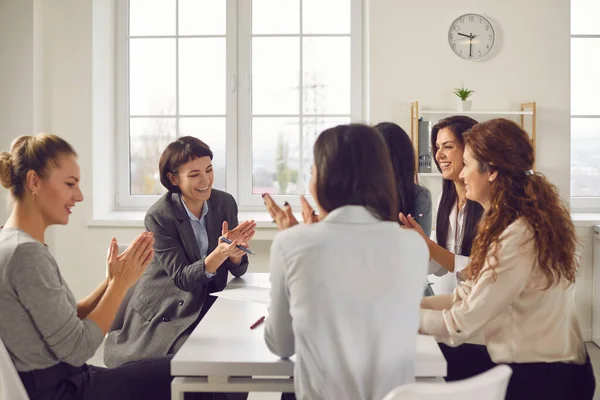 Team of happy business women sitting around office table and applauding each other