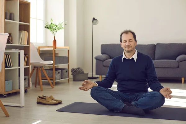 Happy relaxed mature man sitting on floor at home and meditating with eyes closed