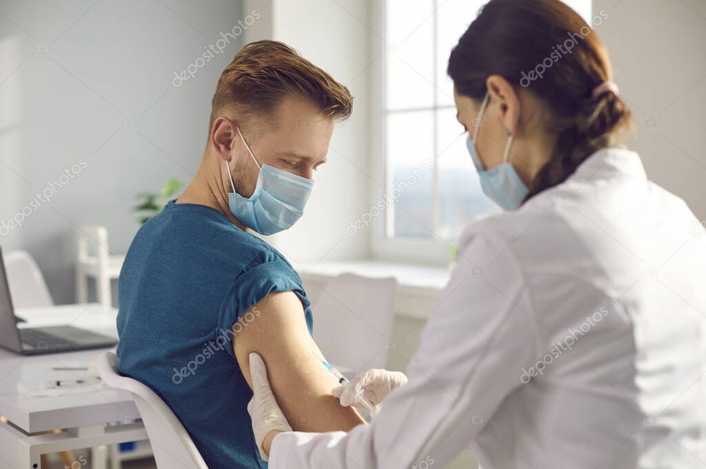 Male patient in medical face mask getting clinical trial vaccine during virus pandemic