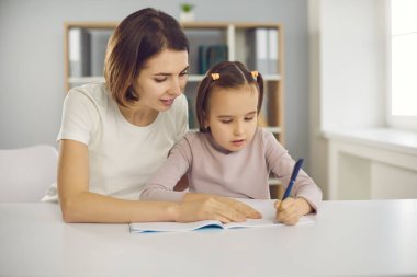 Annesiyle ya da dadısıyla aynı odada oturan ve resim çizen küçük konsantre bir kız.