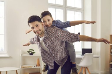 Küçük oğlunu sırtında taşıyan mutlu genç baba evde boş zamanlarının keyfini çıkarıyor.