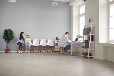 Genç bir kadın ve küçük kızı aşı olmak için sırada bekliyorlar.