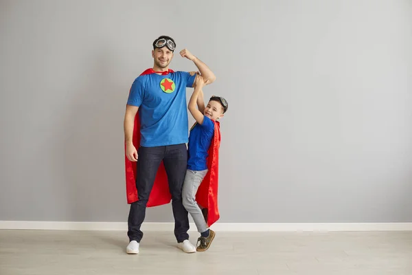Happy young dad and little son dressed in hero capes playing and having fun together