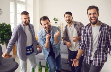 Neşeli genç erkek arkadaşlar evde ayı ve abur cuburla parti yapıp karaoke yapıyorlar.