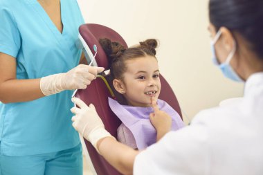 Diş muayenehanesindeki küçük kız iki dişçinin dişlerini gösteriyor..