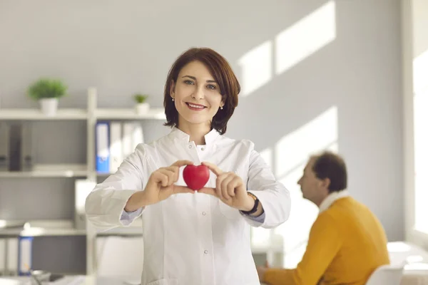 Female cardiologist holding a small red heart as a symbol of a healthy important human organ.