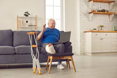 Kırık bacaklı yaşlı adam doktor ya da aileyi arıyor ve dizüstü bilgisayara el sallıyor.