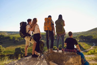 Bir grup turist yaz tatillerinde ayakta, oturarak ve yeşil vadi manzarasının keyfini çıkarıyorlar.