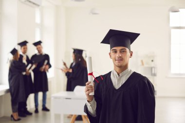 Üniversite mezunu üniformalı, elinde diplomasını gösteren kendinden emin bir öğrenci..