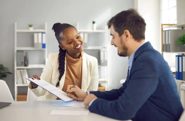 African American female bank manager or financial advisor gives a contract to a client to sign. — Stock Photo, Image