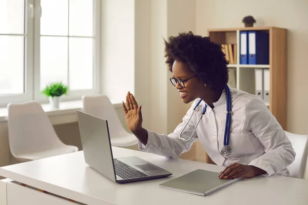 Young dark-skinned female doctor provides an online consultation to the patient via video link.