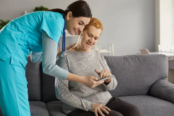 Nurse teaching senior woman to use health monitoring app on tablet or mobile phone