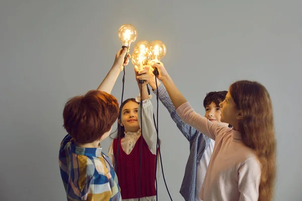 Conceptual studio shot of team of smart little children holding glowing light bulbs