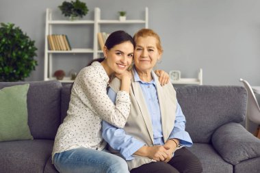 Yetişkin kızıyla birlikte kanepede oturan mutlu kıdemli annenin portresi.