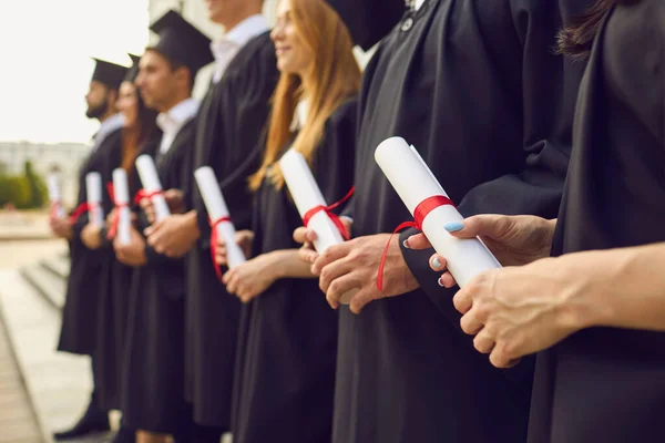 Концепція аспірантури. Обрізане зображення ряду студентів у чорному одязі з дипломами в руках на церемонії випуску — стокове фото