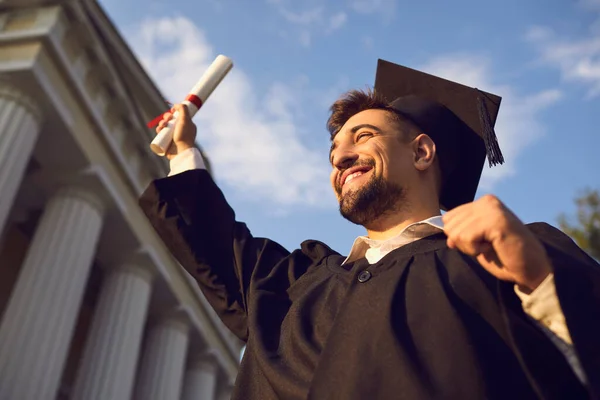 Portrait of overjoyed young graduate holding up his diploma celebrating college graduation