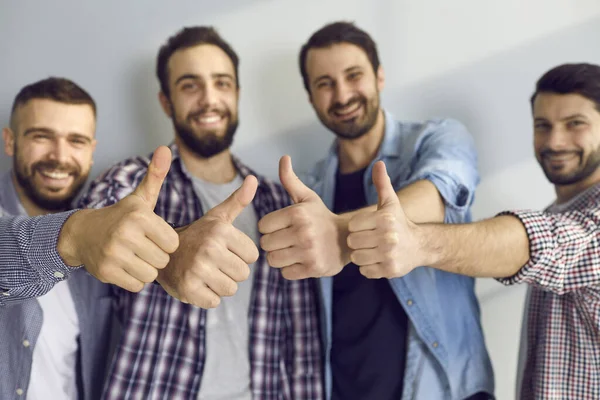 Male friends show pleasure and give a positive feedback showing thumbs up against the gray wall.