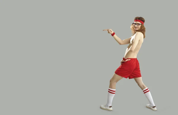 Funny shirtless thin man in sports shorts pointing with finger to advertising copy space
