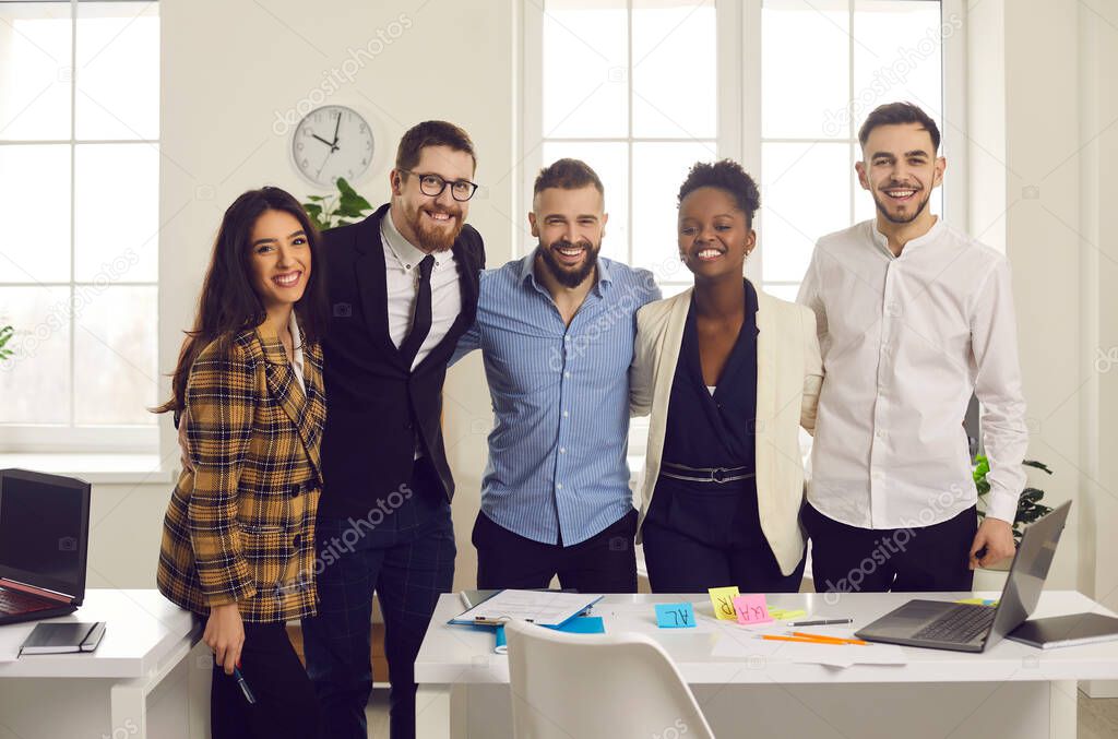 Positive smiling diverse business team hugging looking at camera in office