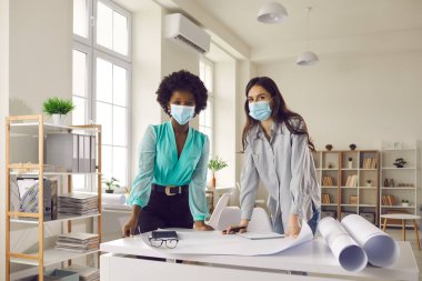 Ofis stüdyosunda duran yüz maskeli tasarımcıların ve iş kadınlarının portresi