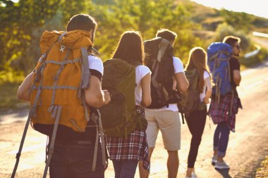 Bir grup genç turist sırt çantalarıyla doğal kayalıklarda yürüyüş yapıyor.