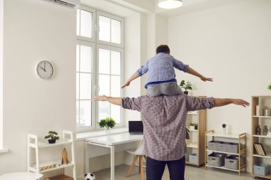 Eğlenceli bir aile. Küçük çocuk babasının omuzlarına oturur ve bir uçuşu taklit ederken eğlenirler..