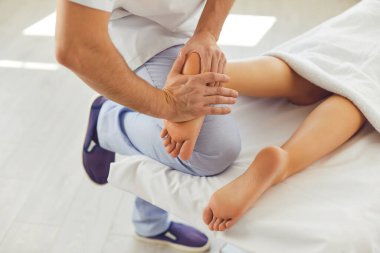 Modern sağlık kliniğinde genç bir kadına ayak masajı yapan profesyonel bir masör.