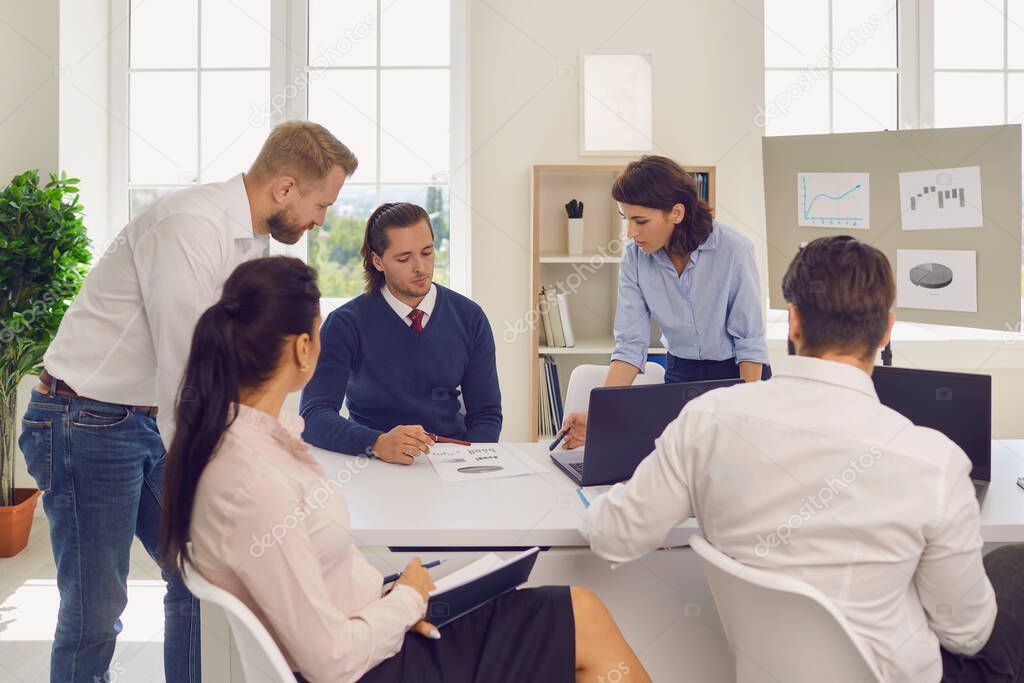 Department manager holding meeting with employees and analyzing financial reports in modern office