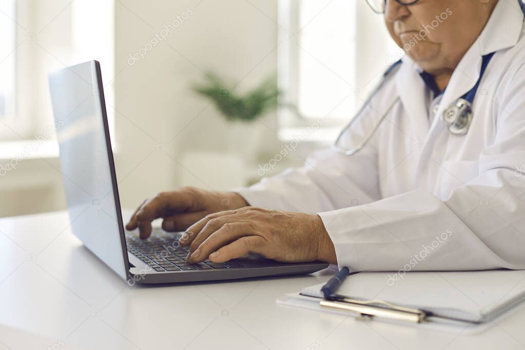 Senior doctor using laptop, giving online consultations to patients or entering data into system