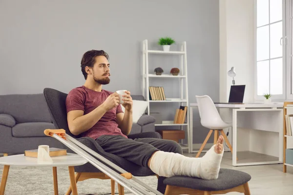 Young man with leg bone fracture feeling sad and bored while staying alone at home