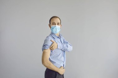 Yüzünde maske olan mutlu bir ofis çalışanının portresi iğneyi vurunduktan sonra kolunu gösteriyor.