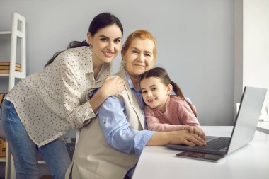 Küçük torunu ve annesi evde dizüstü bilgisayarla çalışan büyükannesine şefkatle sarılıyorlar..