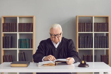 Ciddi bilge kıdemli yargıç mahkemede bir masada oturuyor ve bir kitap okuyor.