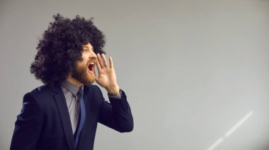 Kıvırcık peruklu komik adam, gri reklam arkaplanda yüksek sesle bağırıyor.