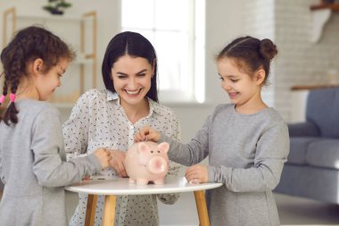 Gri elbiseli mutlu küçük şirin kızlar ve kumbaraya bozuk para koyan genç anneler.
