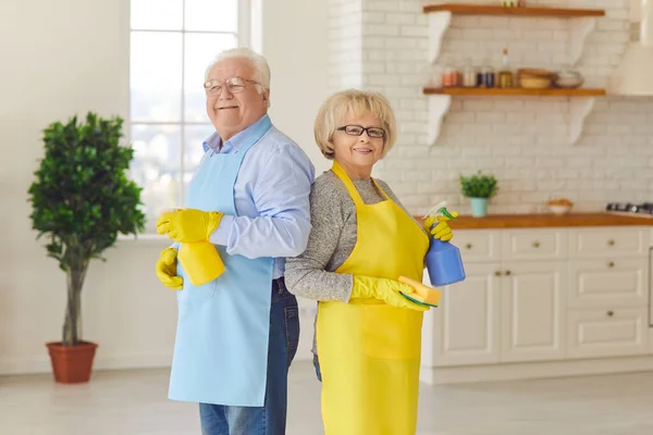 在打扫完房子后，一对老夫妇背靠背地站在厨房里笑得开心极了 — 图库照片