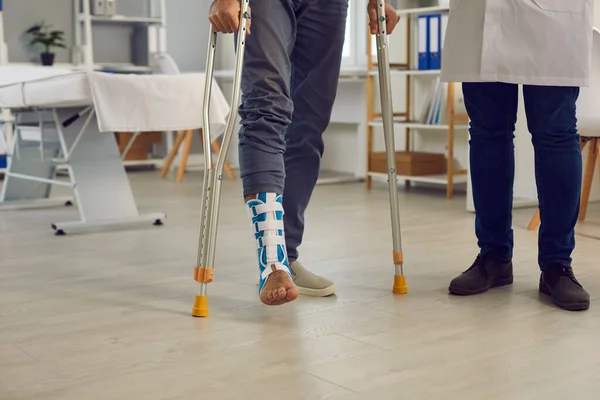 Midsection of patient with injured leg walk with crutches under doctor control