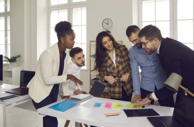Ofiste çalışan işaretli kalem ve çıkartmalarla gülümseyen çok ırklı iş adamları.