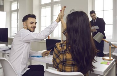 Modern ofiste masada oturan iki mutlu genç birbirine beşlik çakıyor.