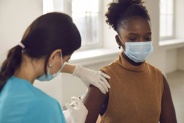 Femme afro-américaine patiente sous masque protecteur assise recevant une injection de vaccin — Photo