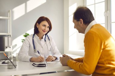 Masasında oturan mutlu dost canlısı doktor, kıdemli hastasına bakıyor ve gülümsüyor.