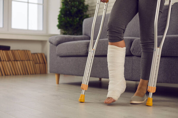 Woman standing with metal medical elbow crutches and showing broken injured leg